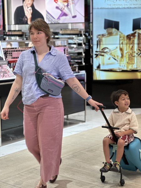 A parent walks through a mall pulling their young son on a wheeled scooter — the kind of small everyday photo a parent already takes.